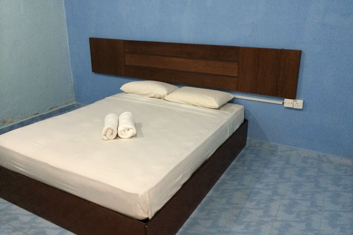 Un lit bien fait, avec du linge de lit blanc et deux serviettes enroulées, une tête de lit en bois et un mur bleu.