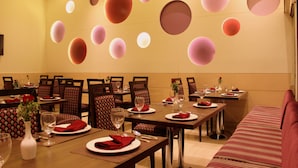 A dining area with round tables, chairs, and a sofa. - Hotel Amrapali Grand (New Delhi)