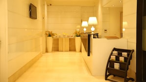 A reception area with a reception desk, two lamps, a wall-mounted TV, and a magazine rack. - Hotel Amrapali Grand (New Delhi)