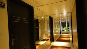 A hotel corridor with a carpeted floor, a glass door, and a potted plant. - Hotel Amrapali Grand (New Delhi)