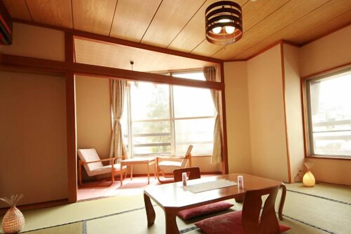 Ein traditioneller japanischer Raum mit Tatami-Boden, einem niedrigen Tisch mit Kissen und Schiebetüren.