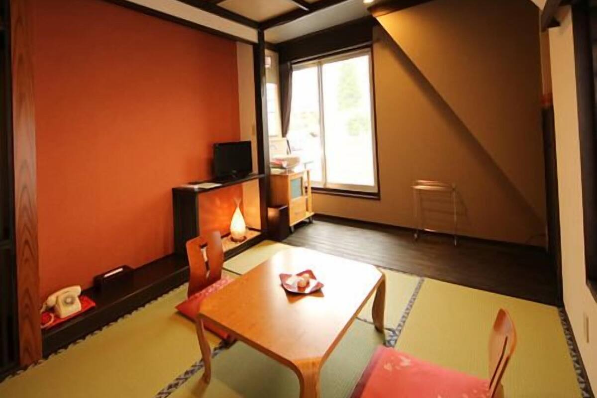 Ein traditioneller japanischer Raum mit Tatami-Böden, einem niedrigen Holztisch und einem Fernseher auf einem Schrank.