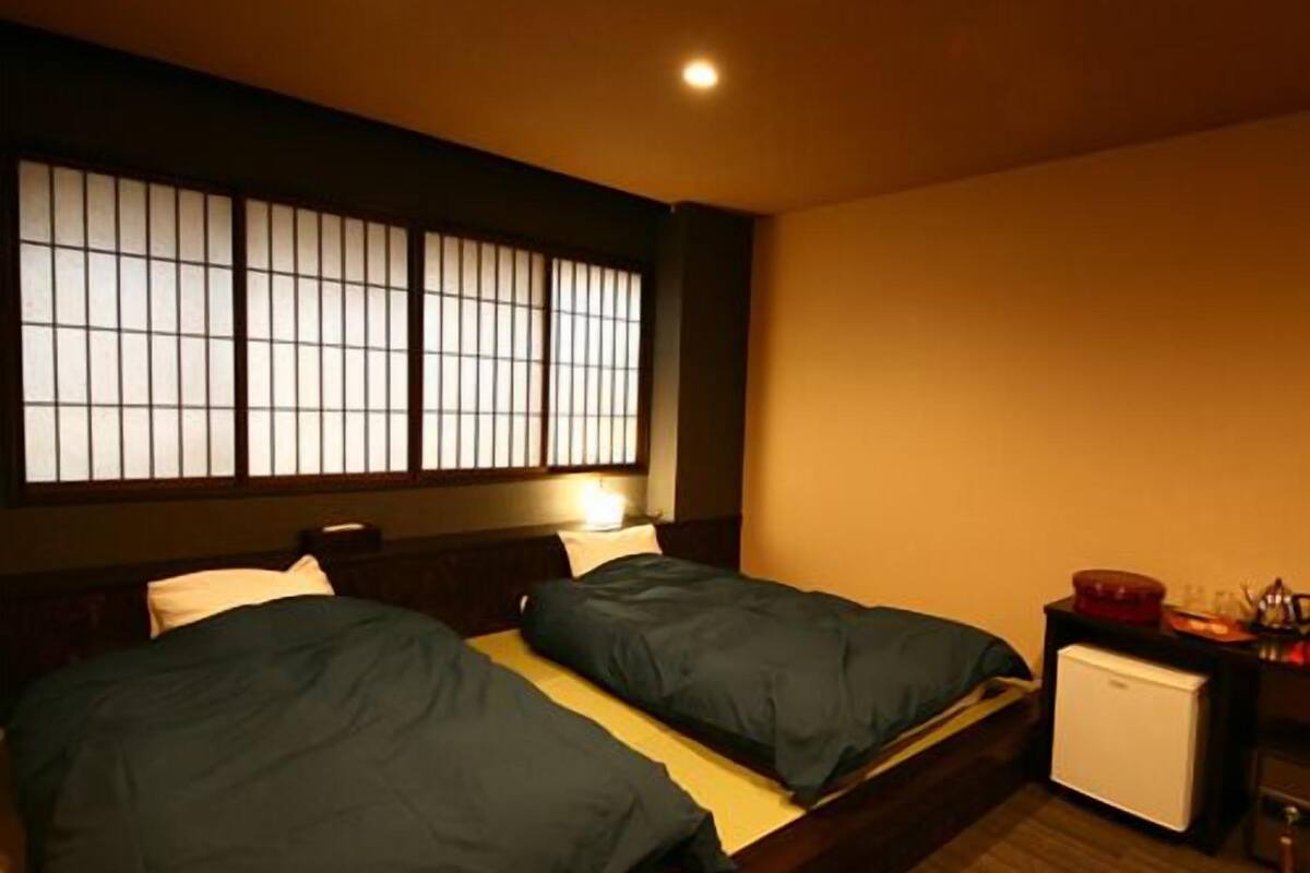 Ein Hotelzimmer mit zwei Betten, einem kleinen Schreibtisch mit Kühlschrank und einem Fenster mit Blick auf die Stadt.