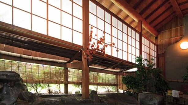 Un onsen japonés tradicional con interior de madera, paredes de piedra y un amplio ventanal.