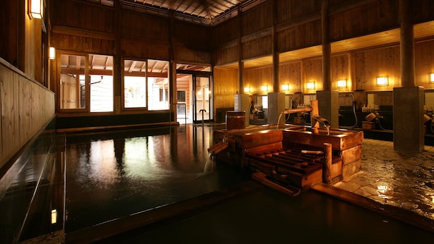 A traditional Japanese onsen with wooden interiors, stone flooring, and multiple hot spring tubs.
