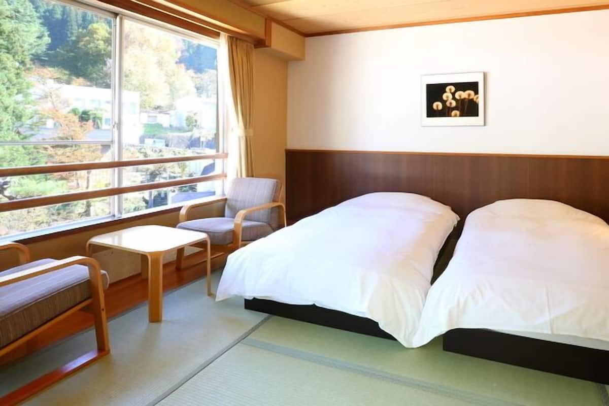 A hotel room with a bed, a chair, a small table, a nightstand, and a picture on the wall.