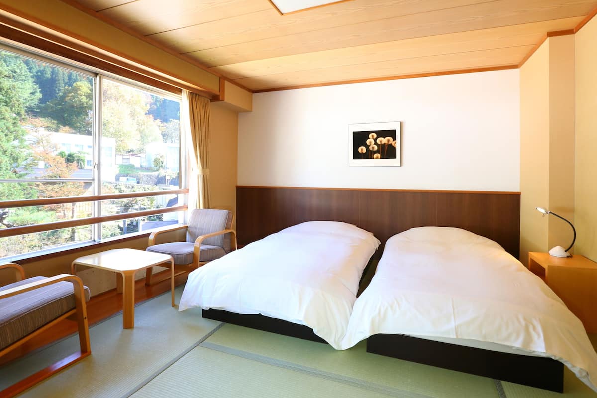 A hotel room with a large bed, a chair, a small table, and a window with a view of trees and buildings.