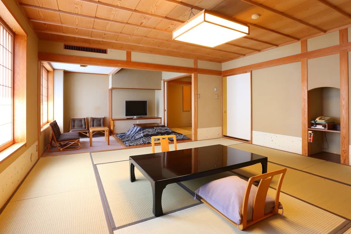 A traditional Japanese room with tatami flooring, a low table, chairs, a television, and sliding doors.
