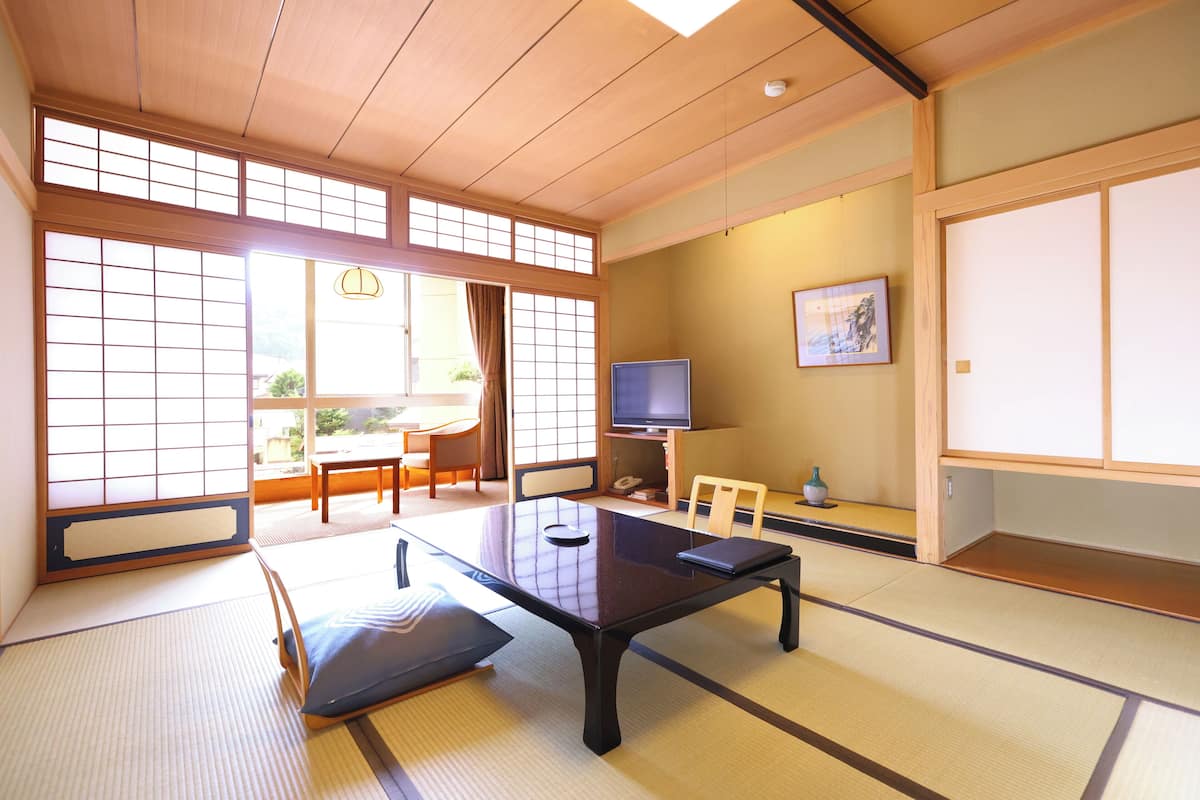 A traditional Japanese room with tatami flooring, a low table, a television, and sliding doors.
