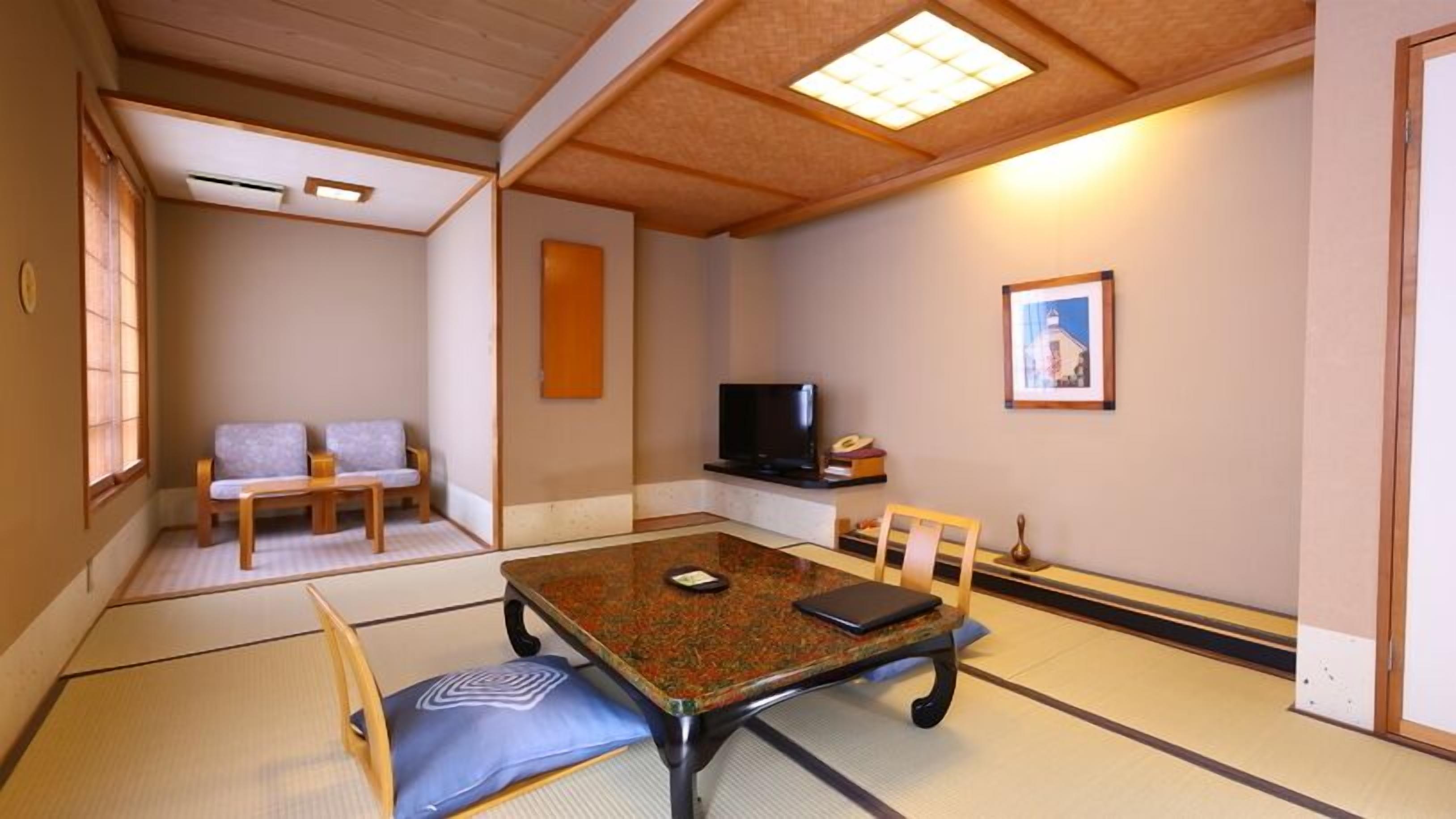 Una habitación tradicional japonesa con suelo de tatami, una mesa baja con cojines, un televisor y un cuadro en la pared.