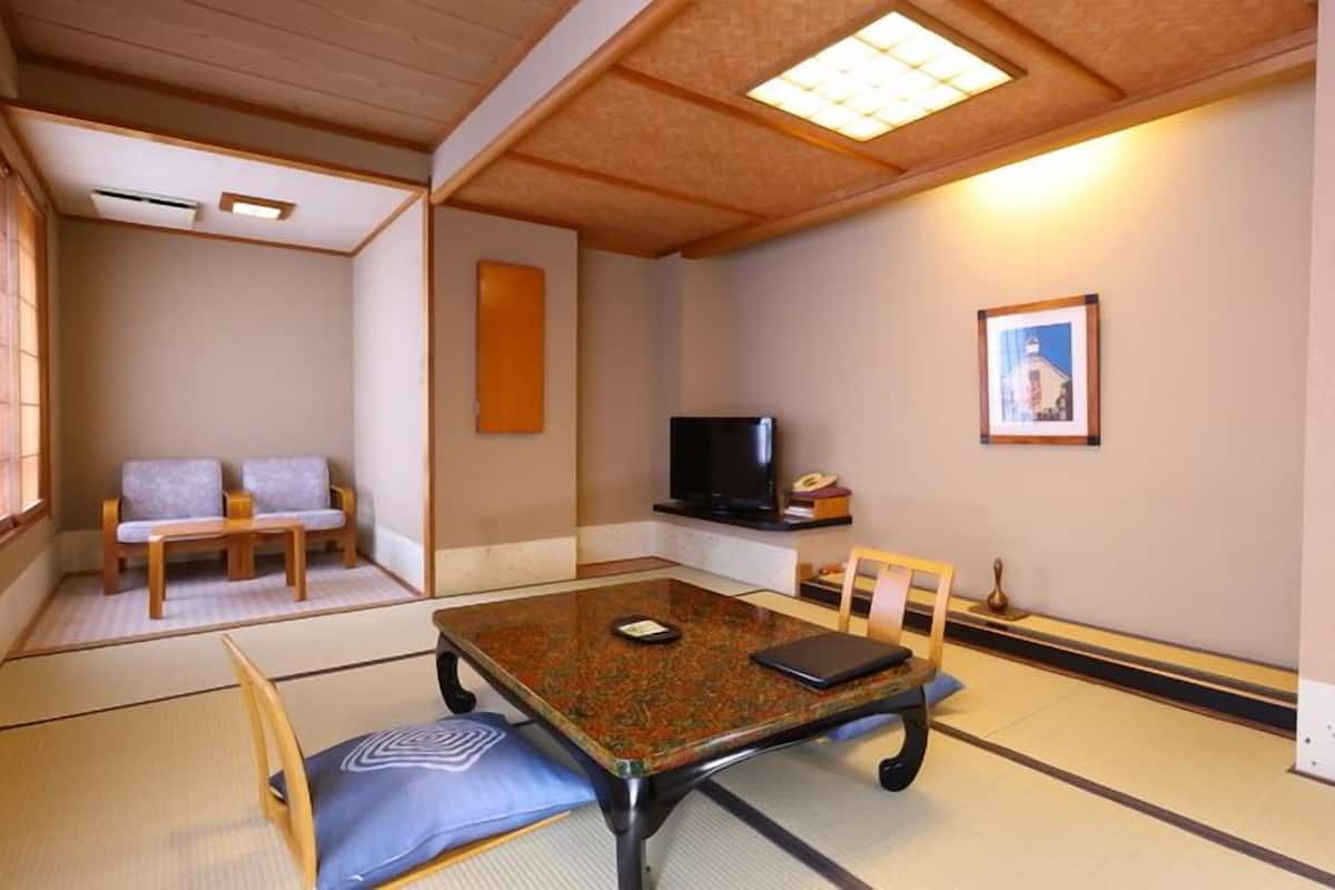 Una habitación tradicional japonesa con suelo de tatami, una mesa baja con cojines, un televisor y un cuadro en la pared.