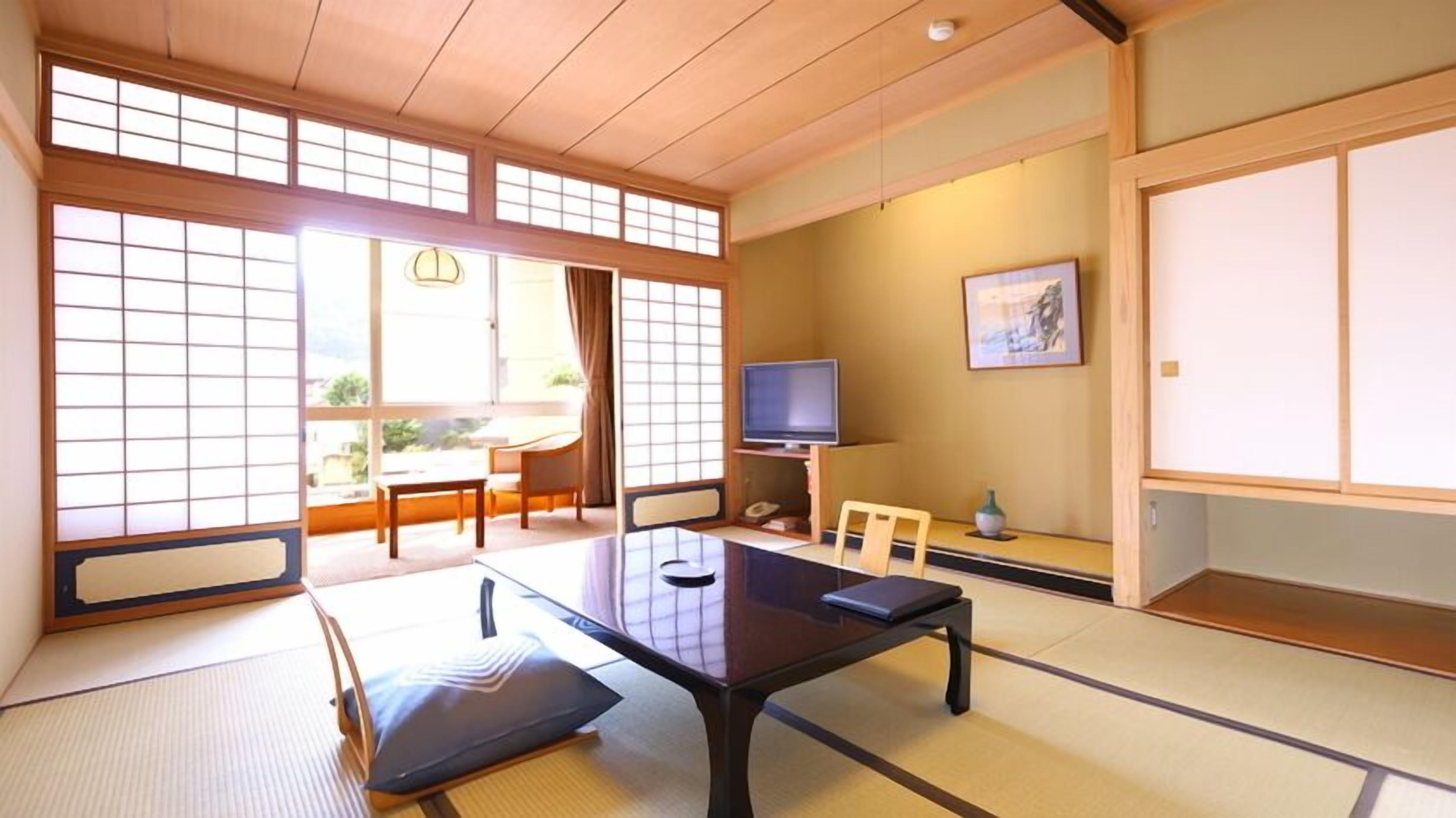 Una habitación japonesa tradicional con suelo de tatami, una mesa baja, un televisor y puertas correderas.