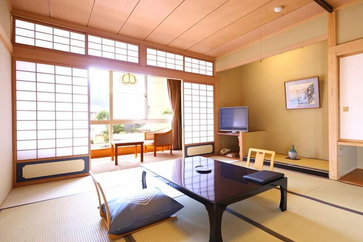 A traditional Japanese room with tatami flooring, a low table, a television, and sliding doors.