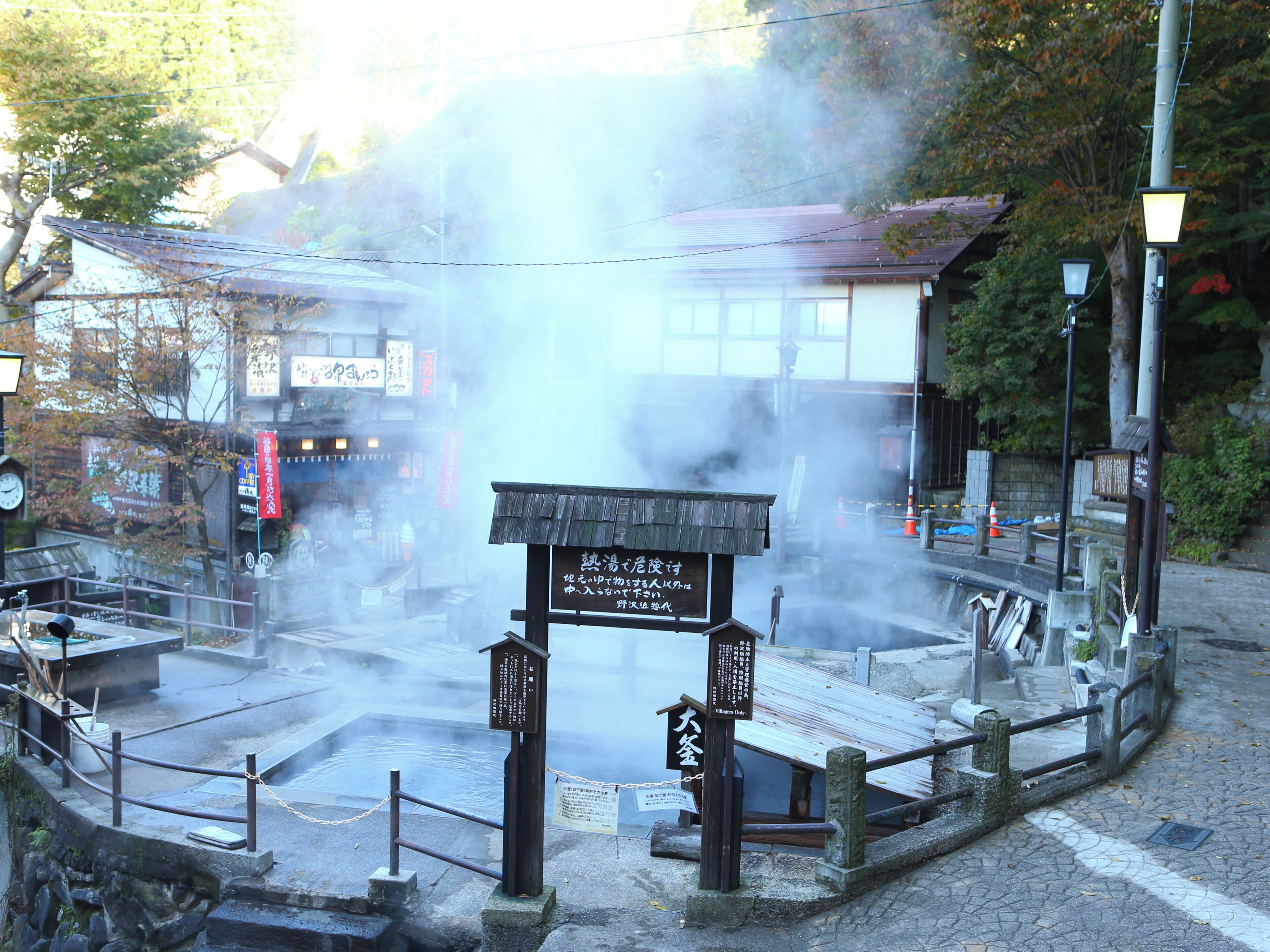 A traditional Japanese hot spring area with a wooden structure, stone steps, and a sign in Japanese.