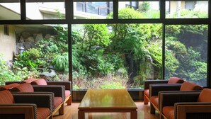 A room with wicker furniture, a wooden table, and a view of a lush garden through large windows.