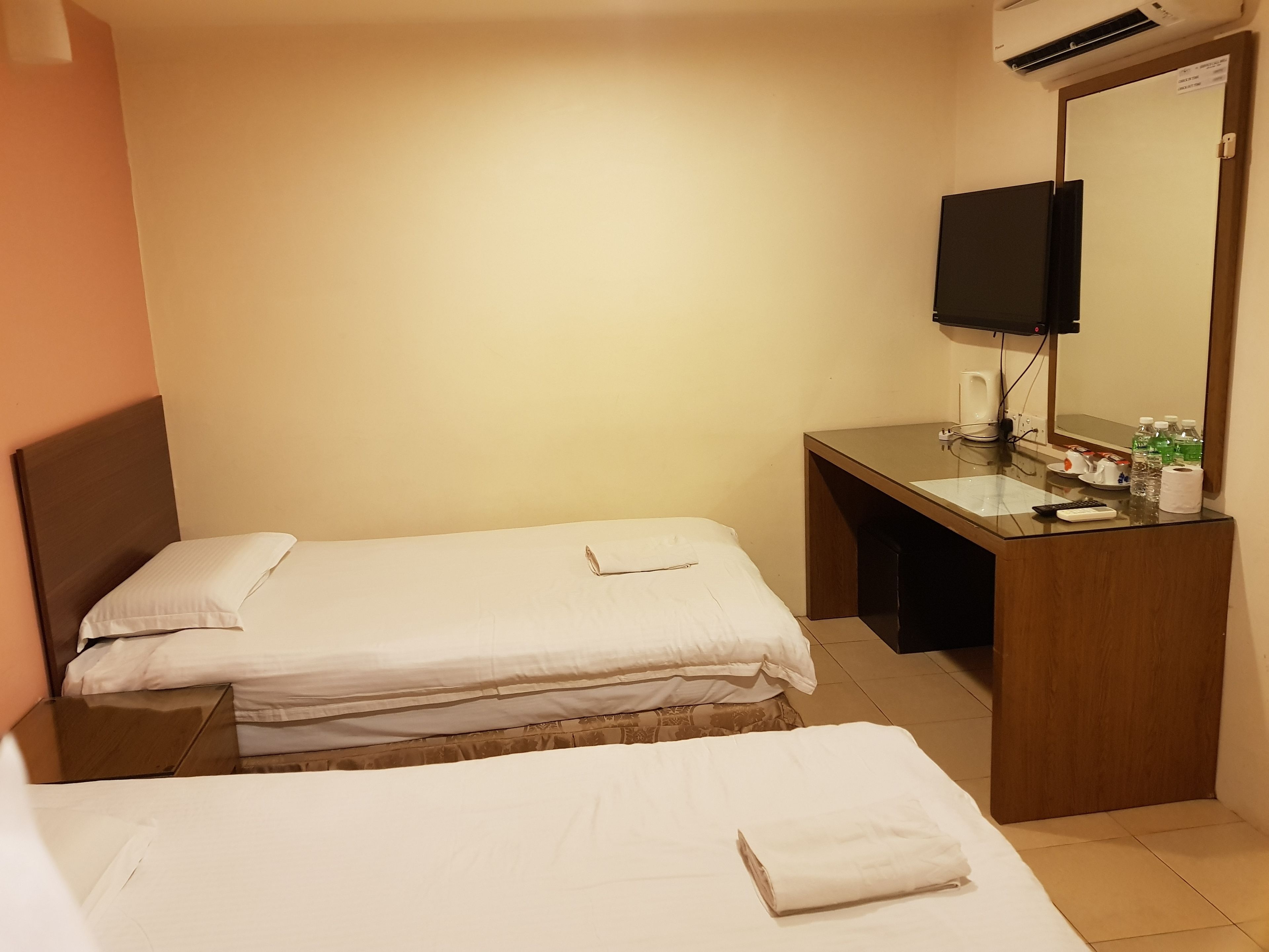 A hotel room with two beds, a wooden desk with a mirror, a television, and toiletries.