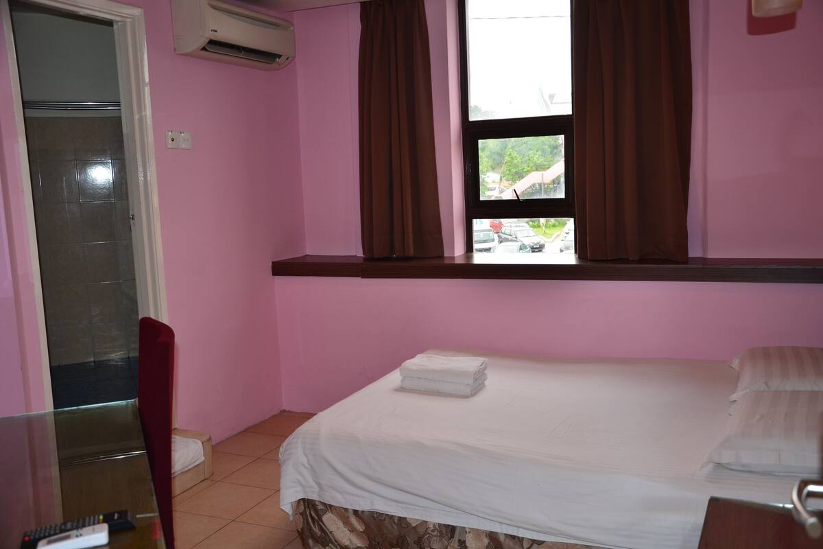 Une chambre à coucher avec un lit, une fenêtre avec des rideaux, une chaise et un appareil de climatisation.