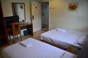 Une chambre d’hôtel avec deux lits, un bureau avec un ordinateur, un miroir et une porte donnant sur une salle de bain.