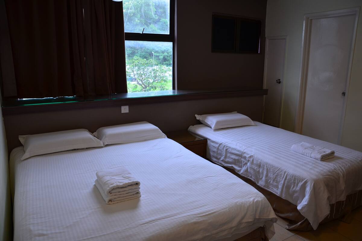 Une chambre d’hôtel avec deux lits simples, une fenêtre avec des rideaux, une porte et une petite fenêtre au-dessus de la porte.