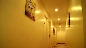 Un couloir étroit et bien éclairé, avec des portes d’un côté et une œuvre d’art accrochée au mur de l’autre.