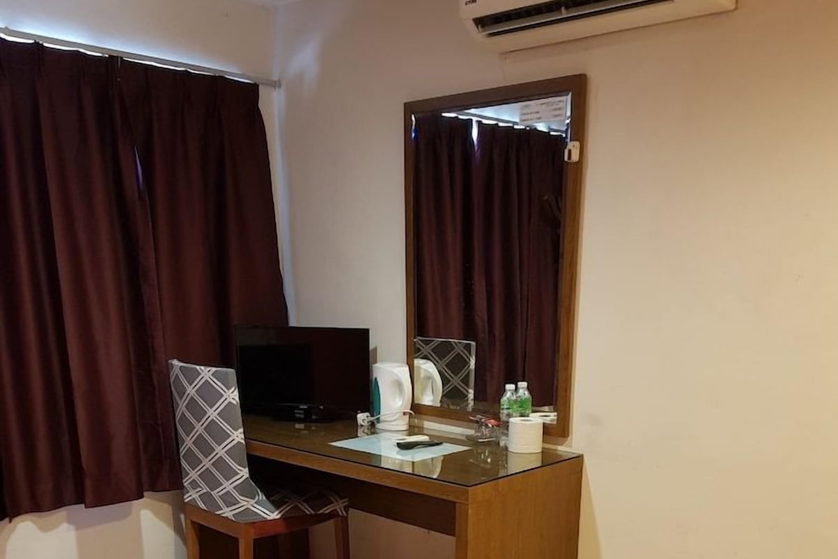Une chambre d’hôtel comprenant un lit, un bureau avec une chaise, une télévision, un miroir et une fenêtre avec des rideaux.