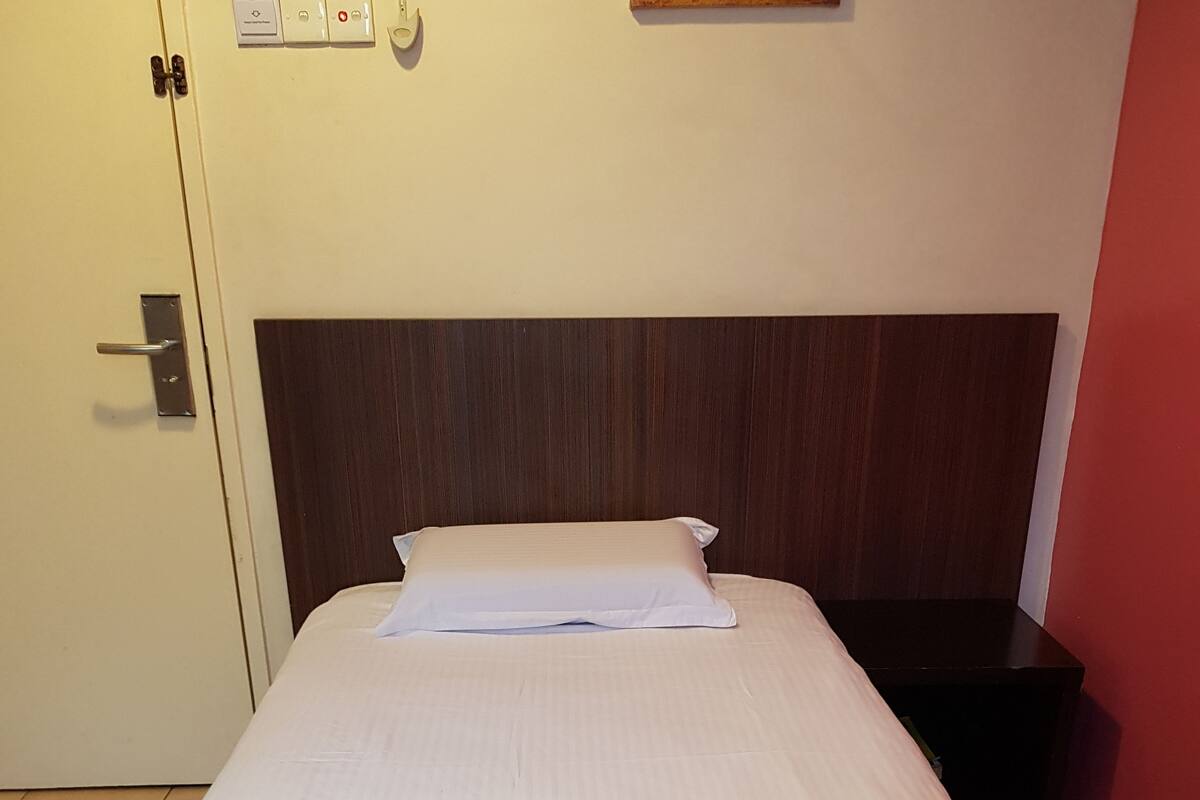 Un lit bien fait, avec du linge de lit blanc et une serviette pliée, une tête de lit en bois, une table de chevet et une porte avec une poignée.