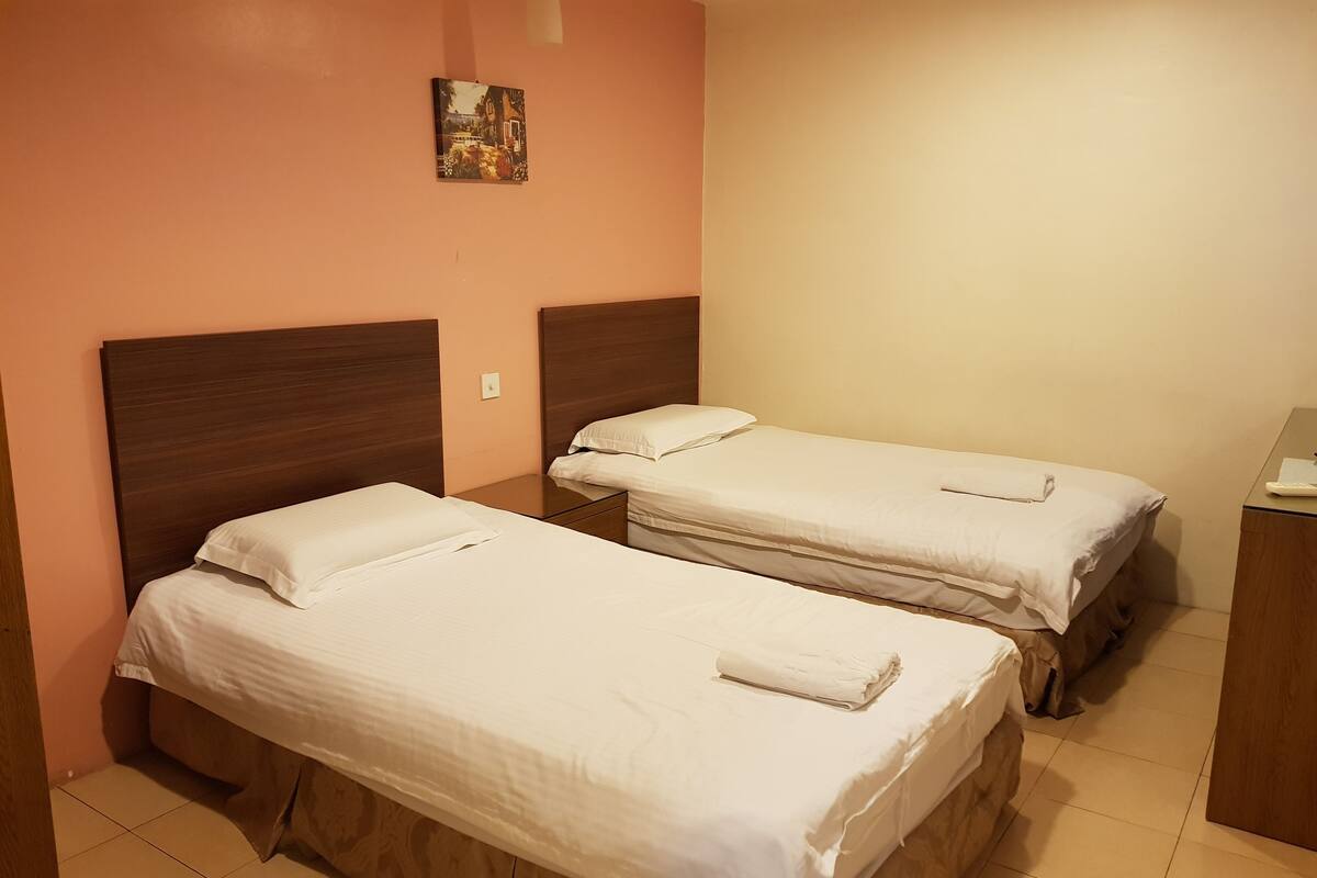 Une chambre d’hôtel avec deux lits simples, une petite table de chevet, une commode et un tableau accroché au mur.