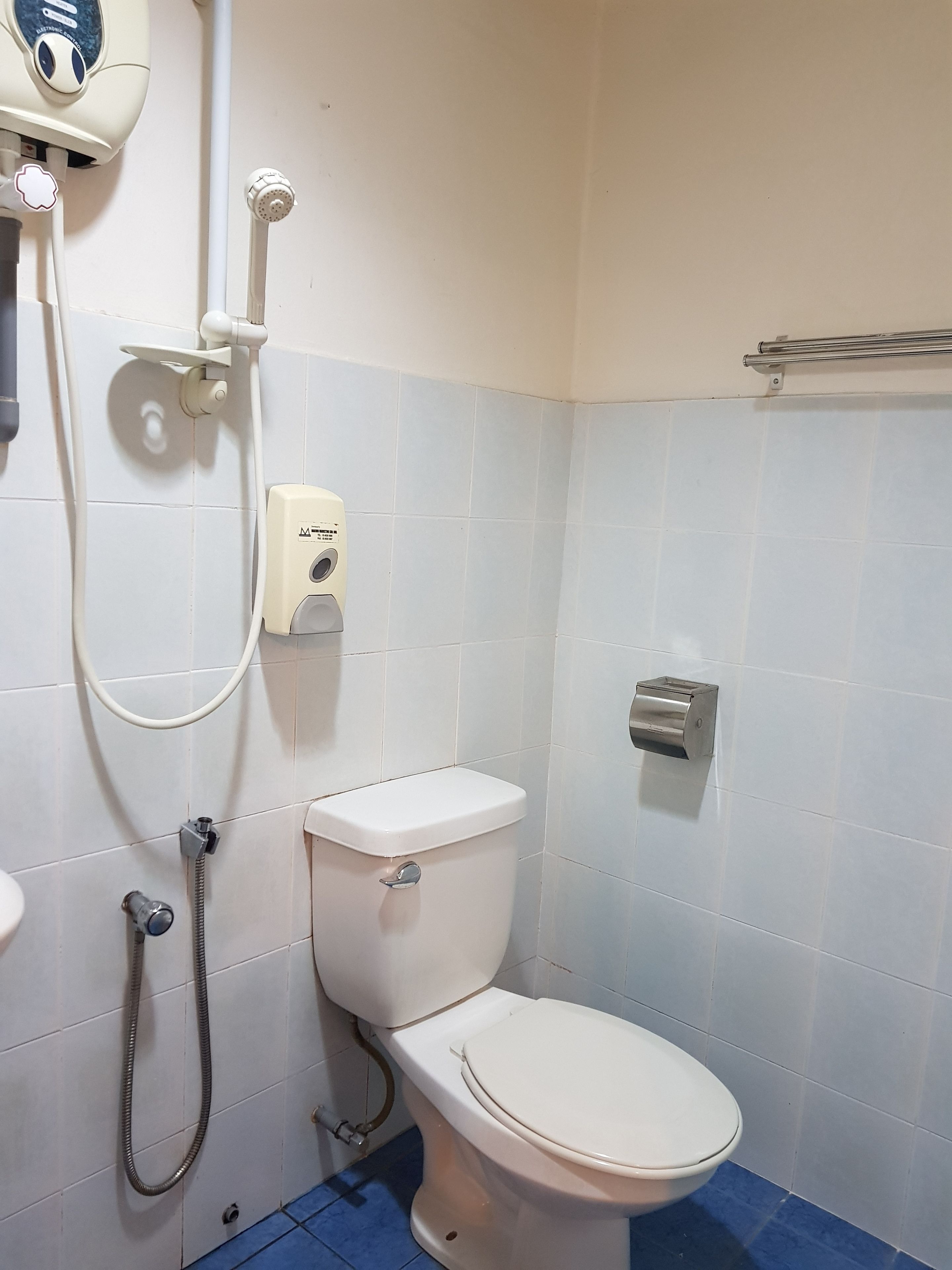 A bathroom with a toilet, a handheld showerhead, a soap dispenser, and a paper towel dispenser.