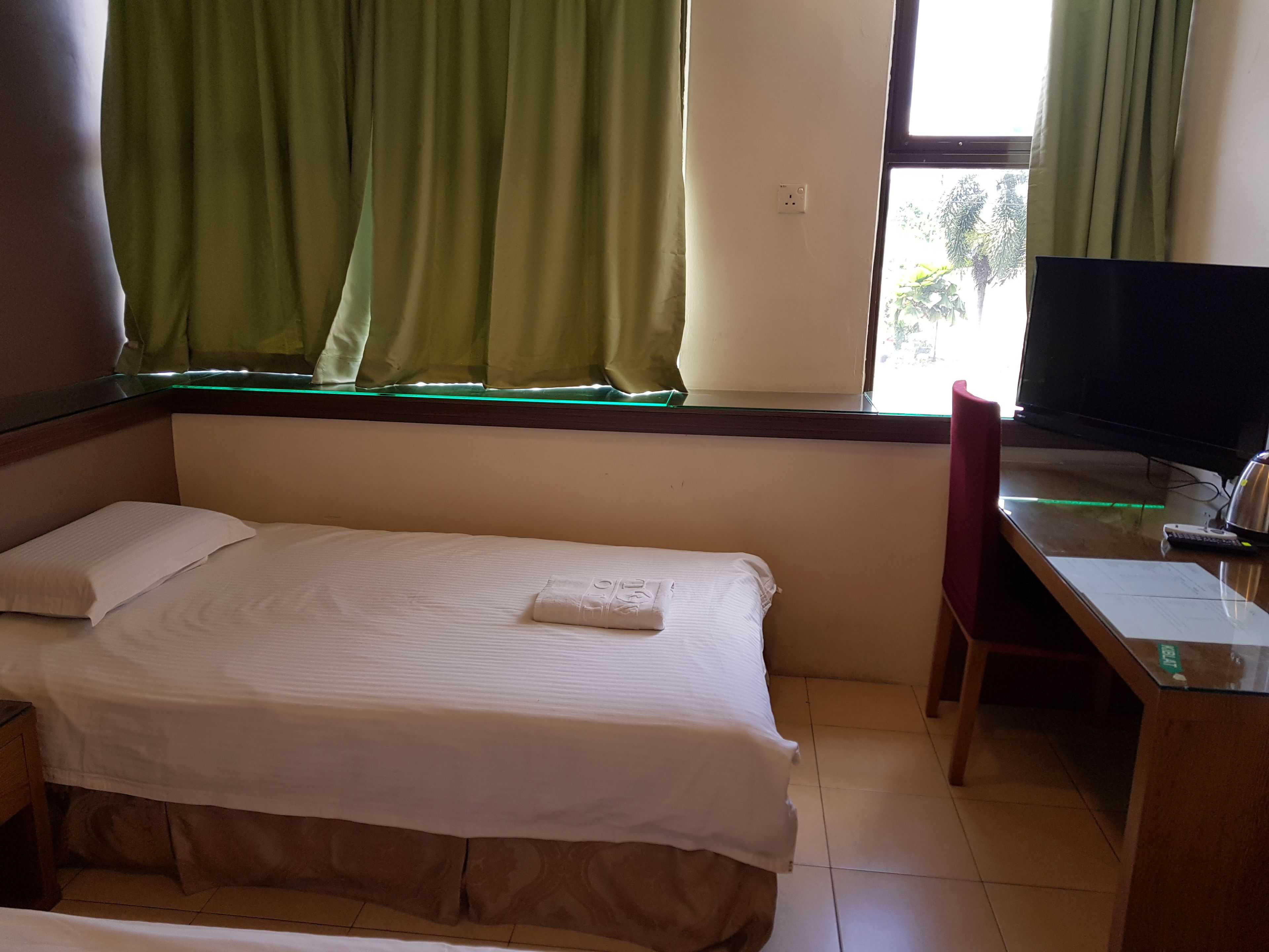 Une chambre d’hôtel avec un lit, un bureau avec un ordinateur, une télévision et une fenêtre avec des rideaux.
