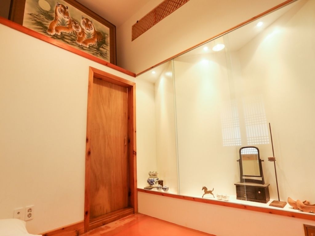 A room with a wooden door, a large mirror, and a small shelf with decorative items.