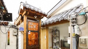 A traditional Japanese building with a wooden door, a small shop window displaying ceramics, and a sign indicating a postal code.