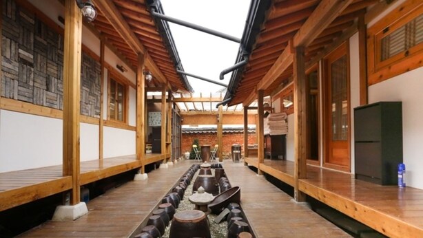 A traditional Japanese-style interior with wooden beams, tatami flooring, and a central pathway with large vases.