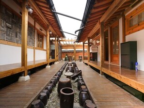 A traditional Japanese-style interior with wooden beams, tatami flooring, and a central pathway with large vases. - TREGA Museum Guesthouse (Jeonju)
