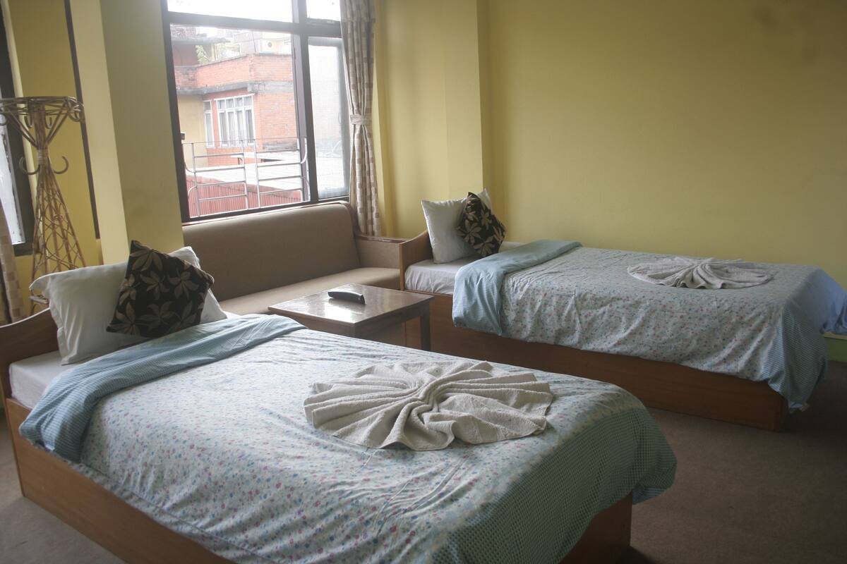 A hotel room with two beds, a small table, and a window with a view of buildings outside.
