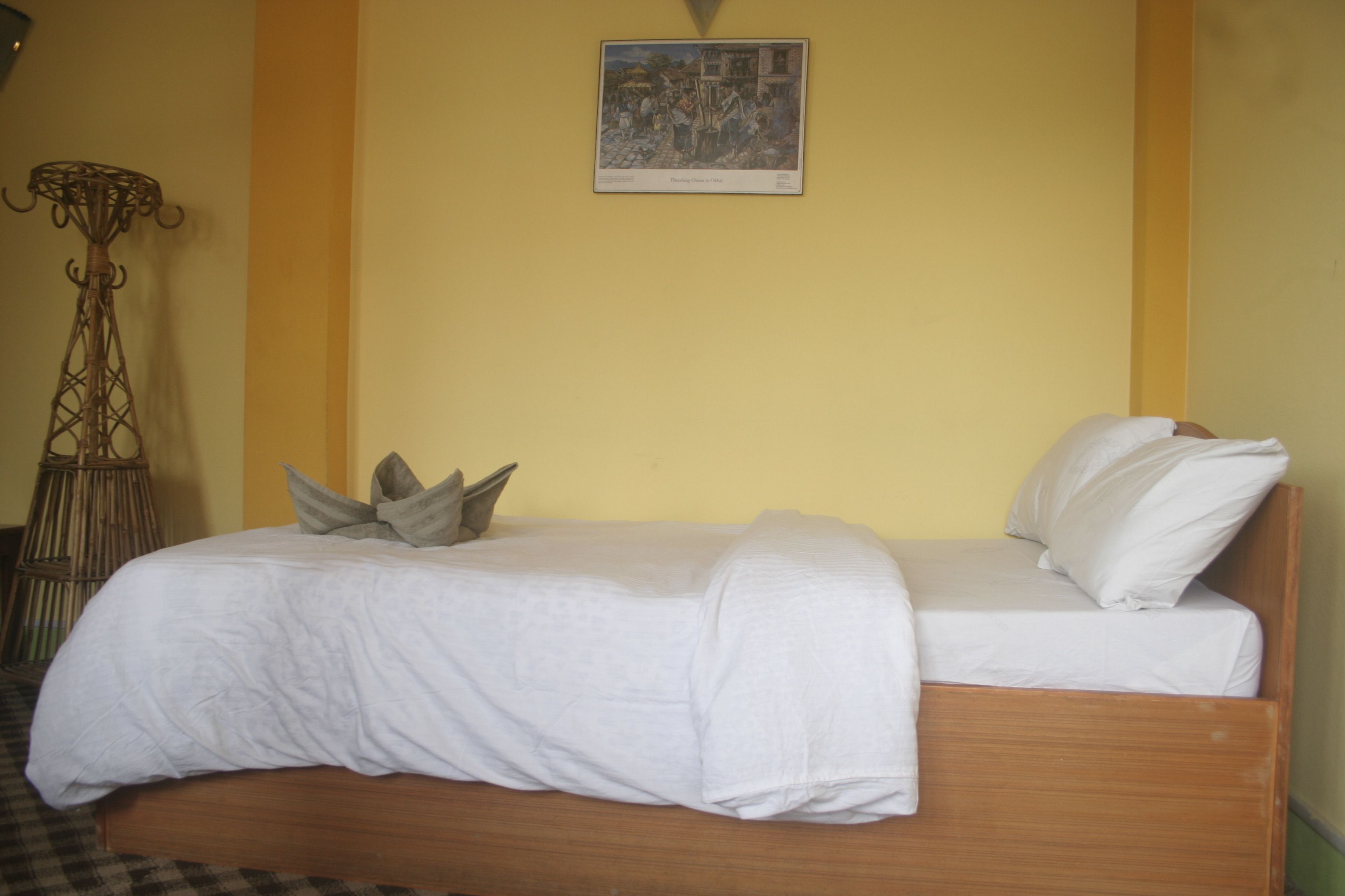 A single bed with a wooden frame, white bedding, and two pillows. There is a wall-mounted picture above the bed.