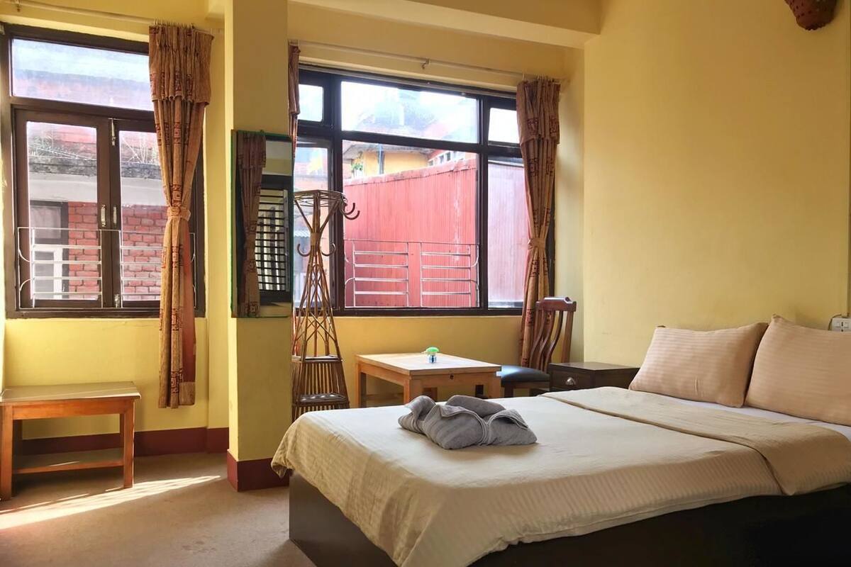 A bedroom with a bed, a small table, a chair, and a window with curtains.