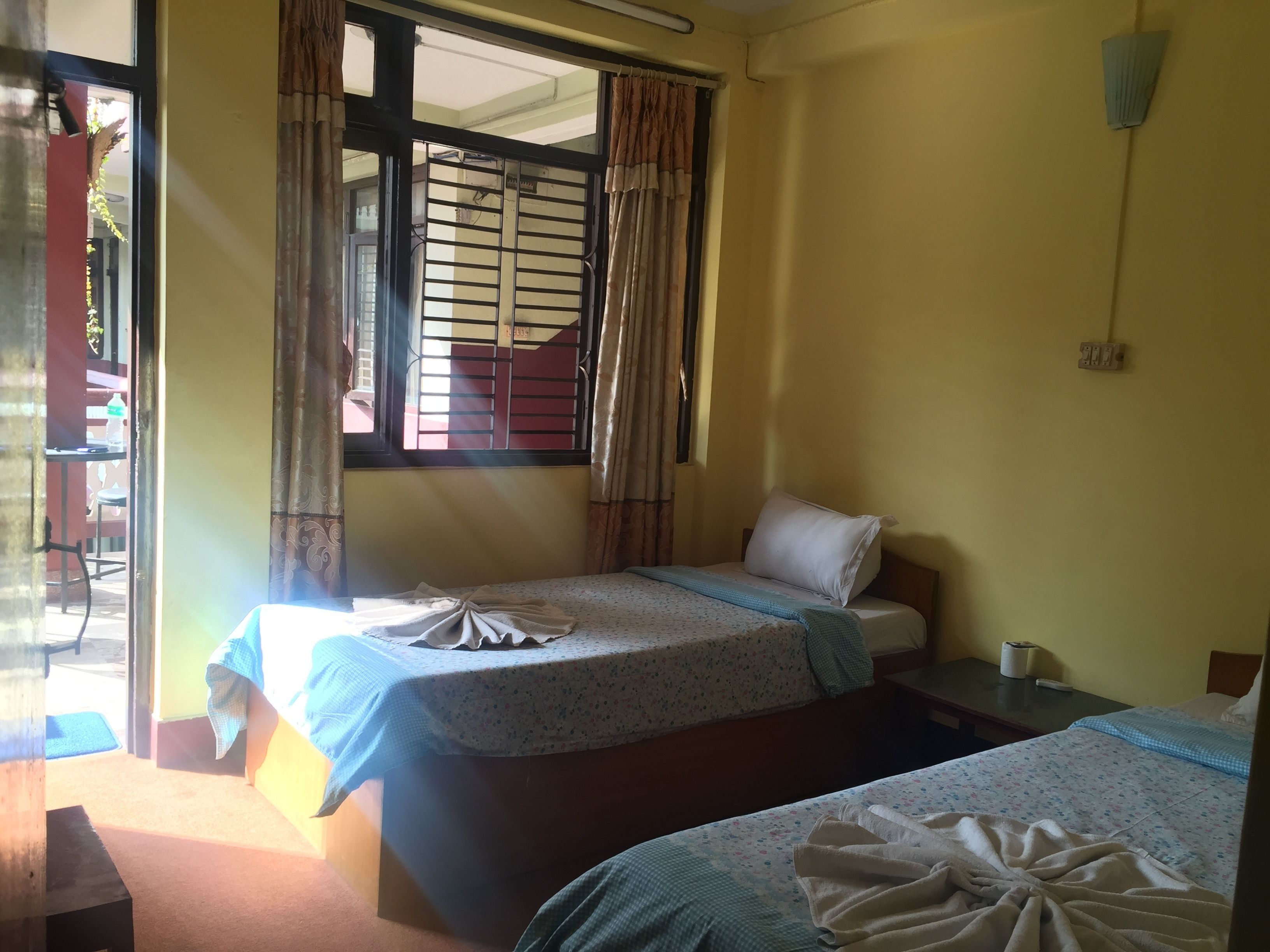 A room with two single beds, a window with metal bars, a small table, and a chair.