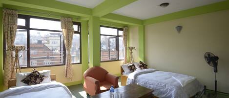 A hotel room with two beds, a wooden table, a chair, and a standing fan.