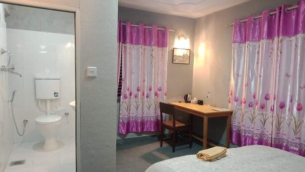 Habitación de hotel con ducha, inodoro, cama, escritorio y cortinas.