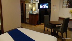 Una habitación de hotel con cama, una mesita, dos sillas, televisor y espejo.
