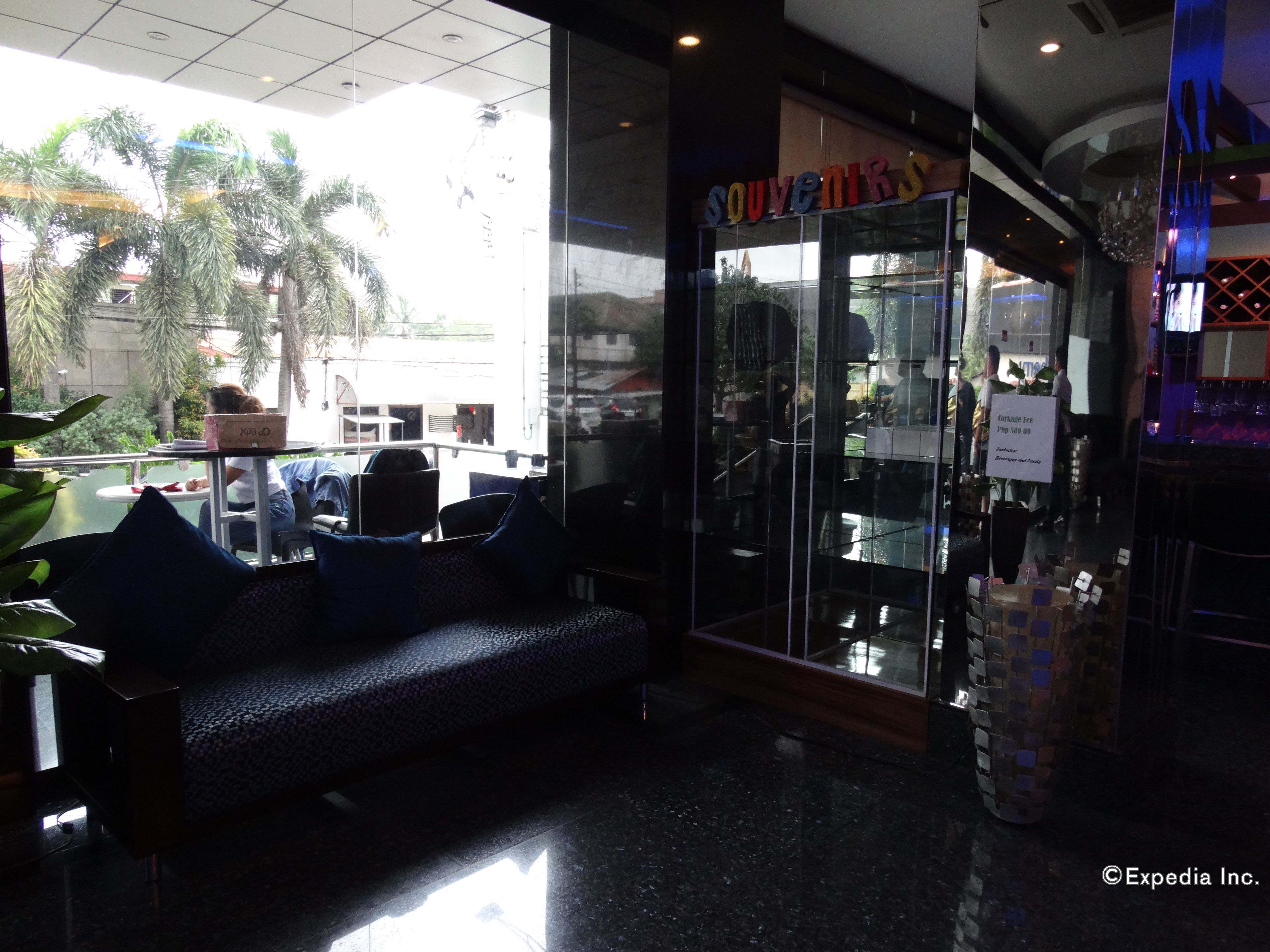 A seating area with a sofa and chairs, a glass storefront with 'SOUVENIRS' signage, and a 'Corkage Fee Php 500.00' sign.