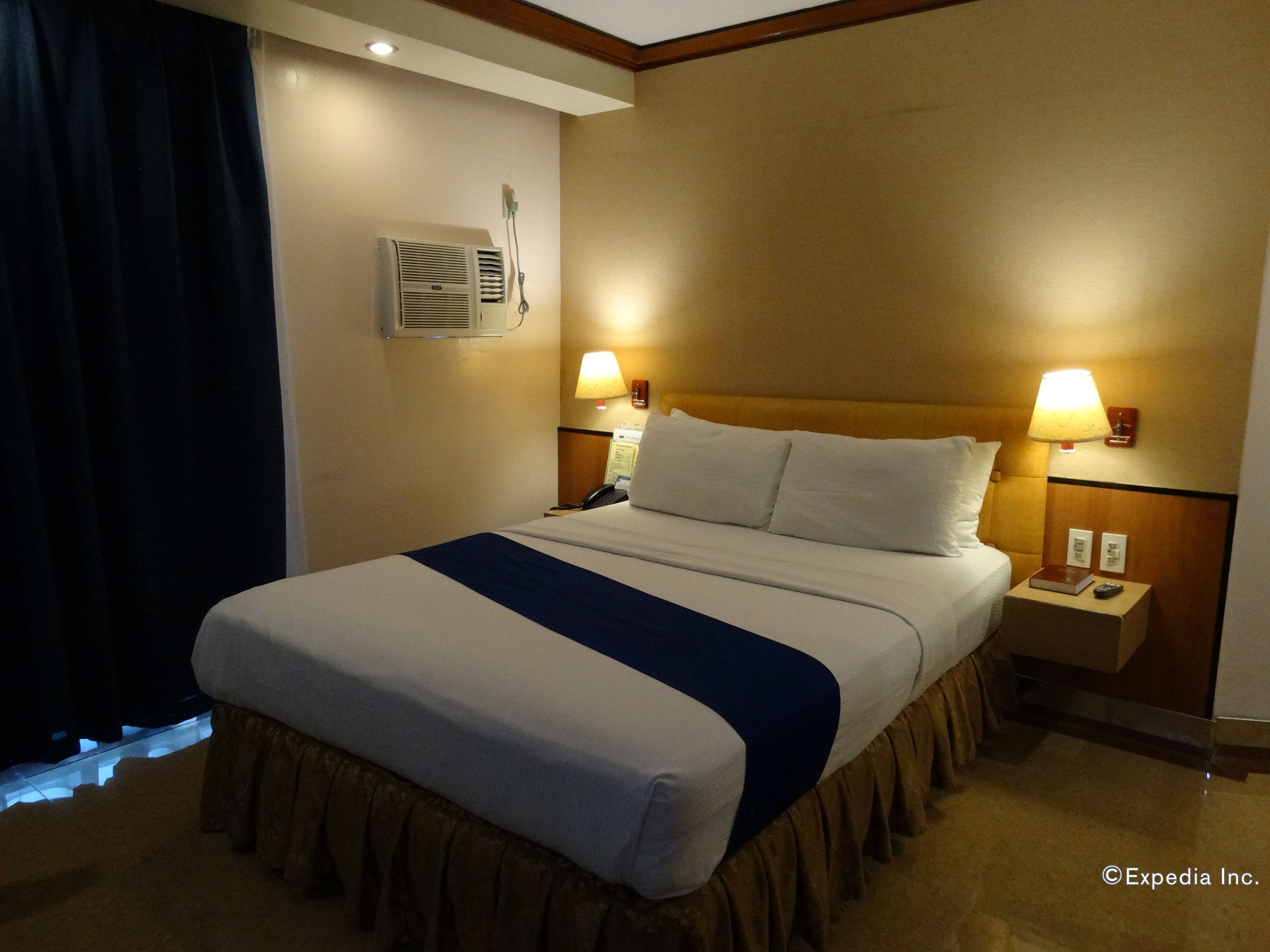 Een hotelkamer met een bed, nachtlampjes, een telefoon en een luchtverkoeler aan de muur.