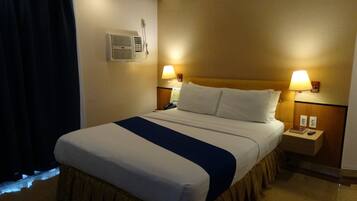 A hotel room with a bed, bedside lamps, a phone, and a wall-mounted air conditioner.