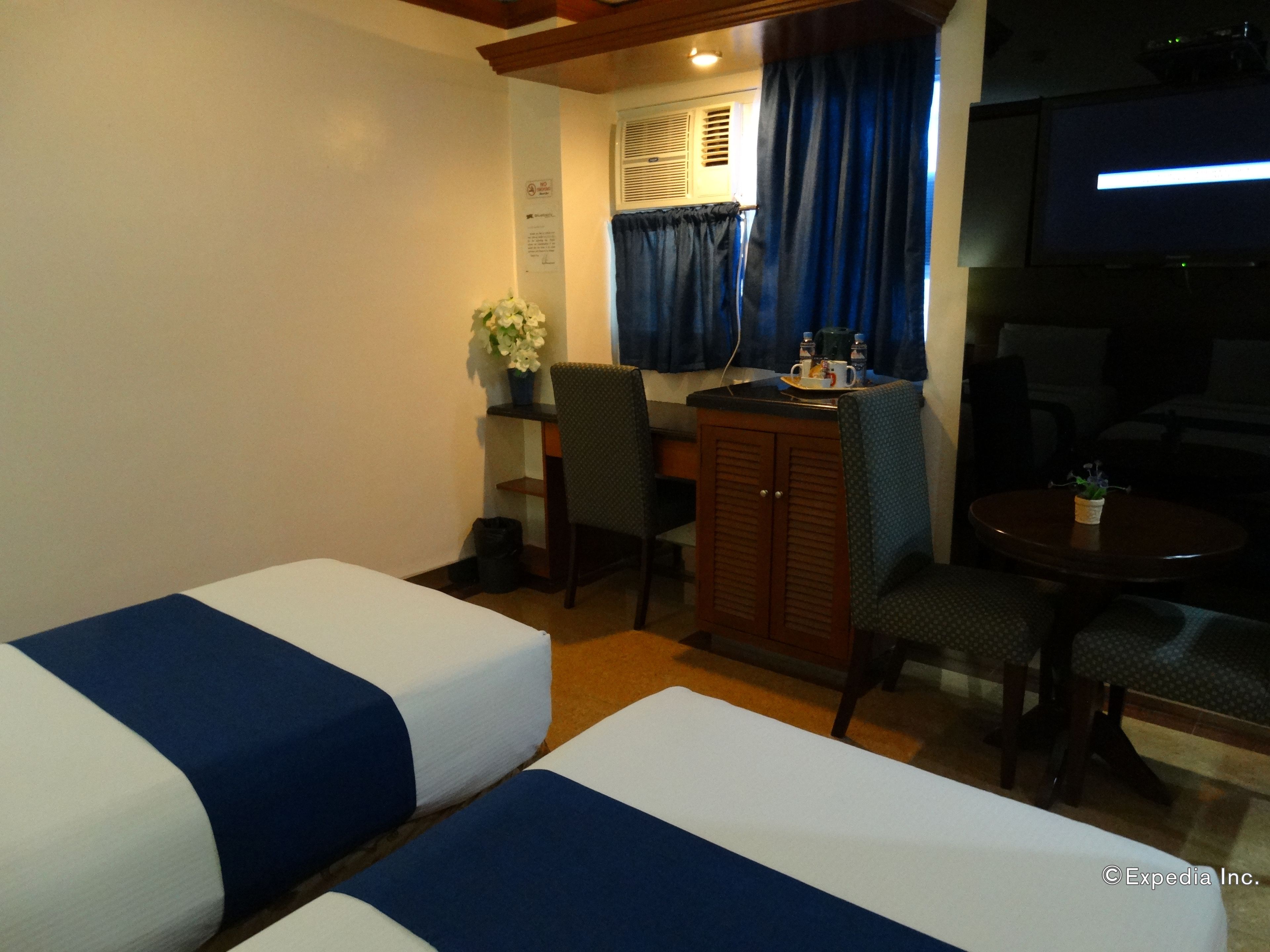A hotel room with two single beds, a small table with a coffee maker, a chair, and a TV.