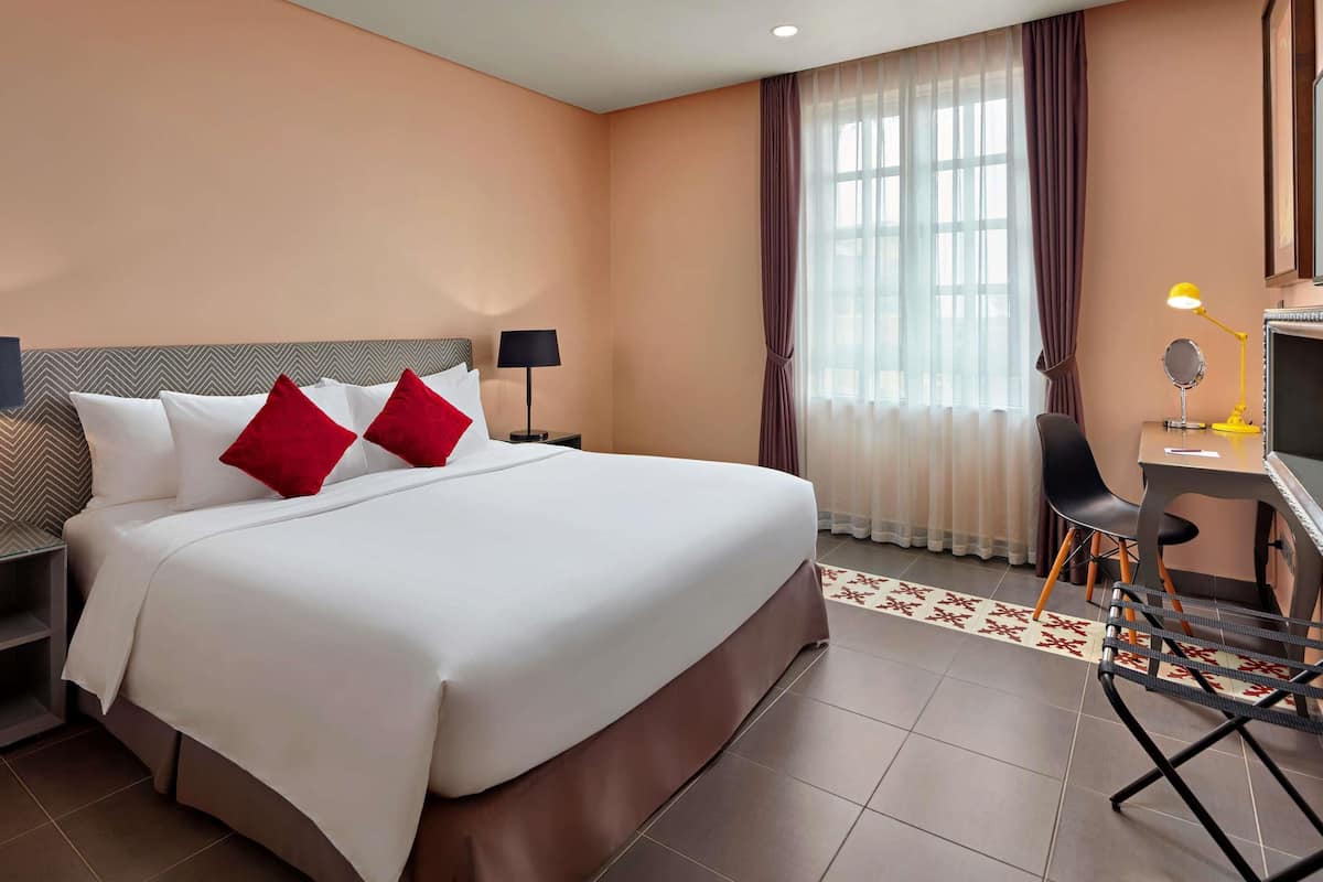 Een hotelkamer met een groot bed, een bureau met stoel, een nachtkastje en een raam met gordijnen.