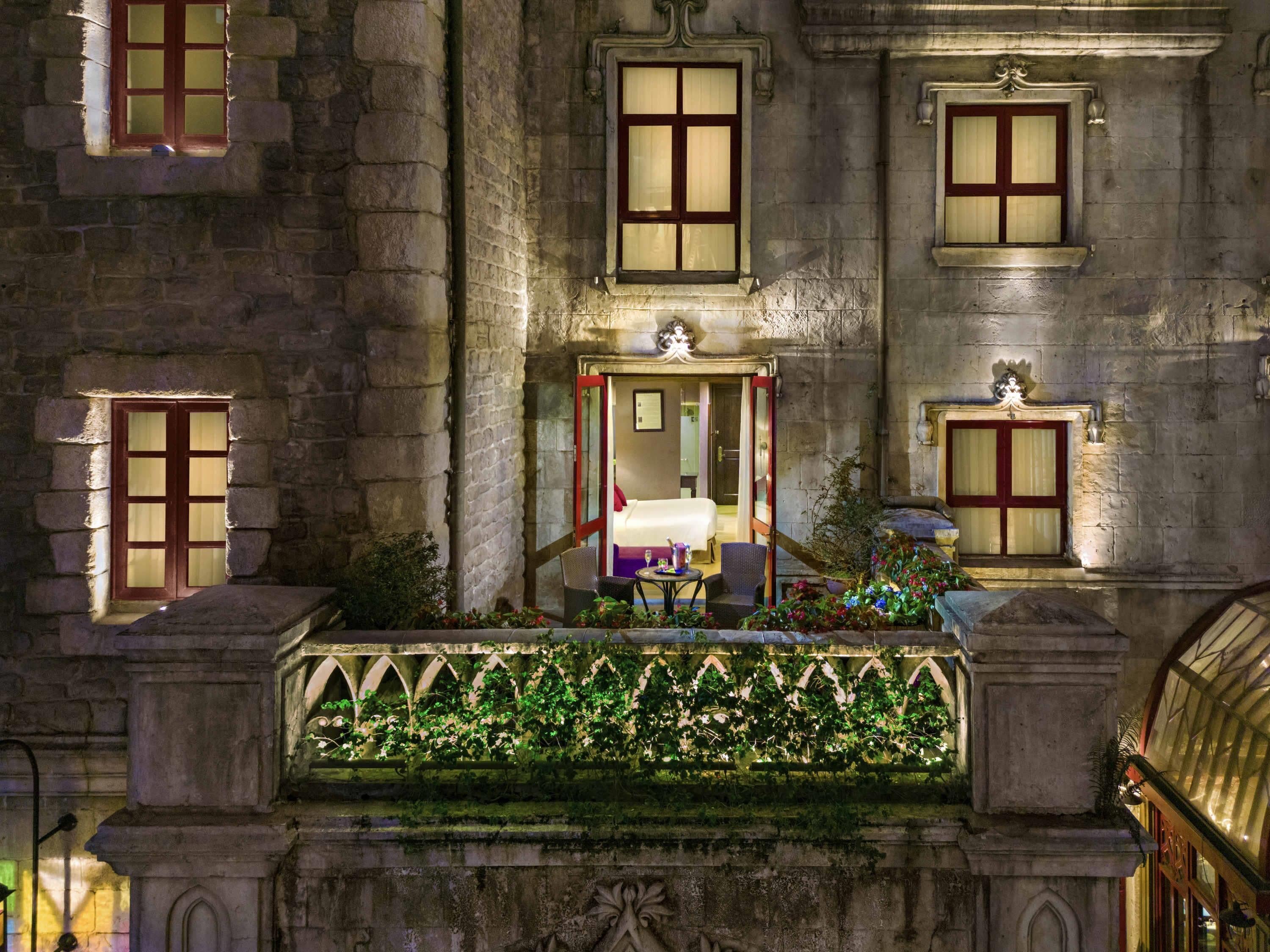 Ein historisches Gebäude mit einem zentralen Eingang, mehreren Fenstern und einem Balkon mit Pflanzen.