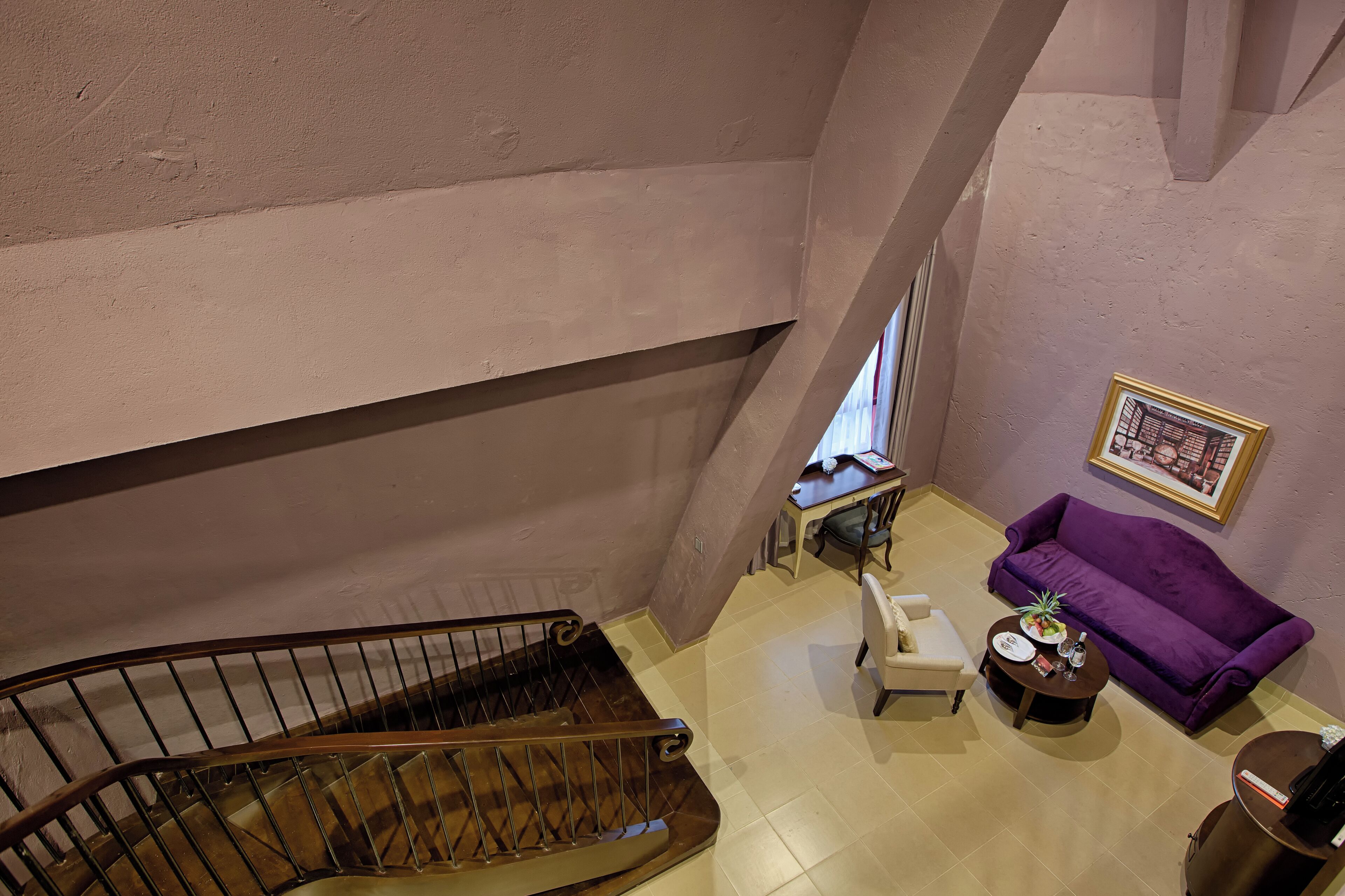 A spacious room with a wooden staircase, a purple sofa, a small table with a plant, and a framed picture on the wall.
