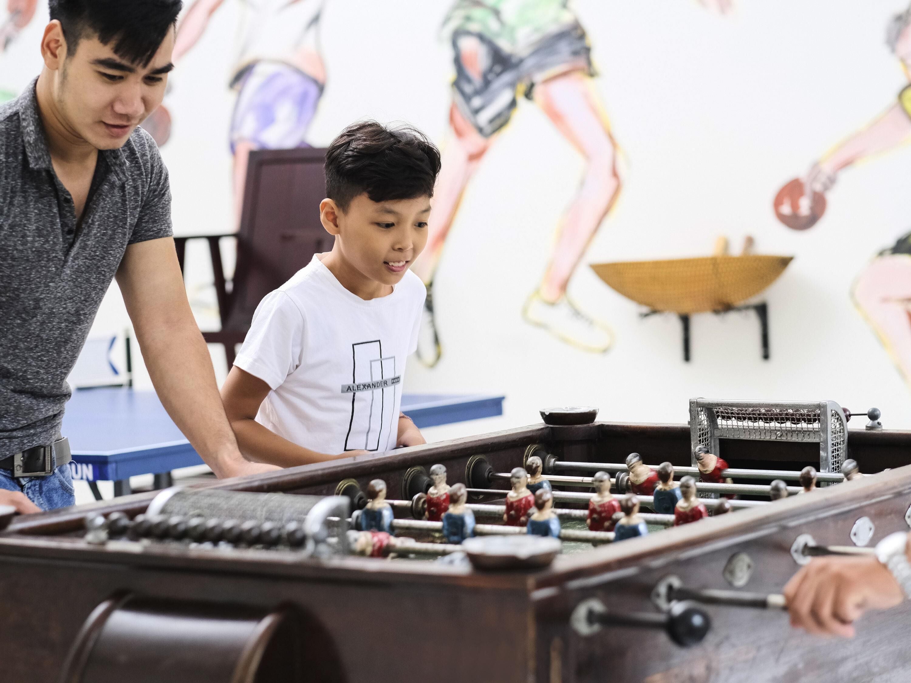 A foosball table with a player wearing a white shirt and a man standing beside it.