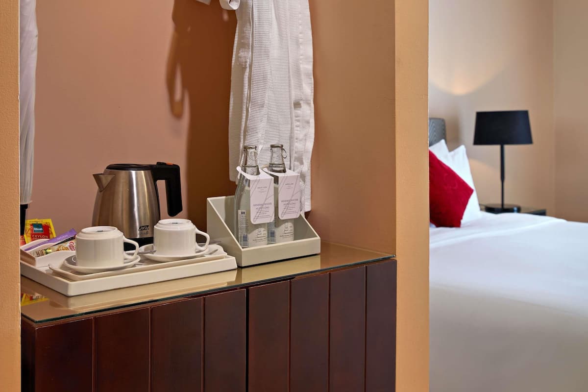 Een hotelkamer met een minibar, een bed, een nachtkastje en een opbergmap.