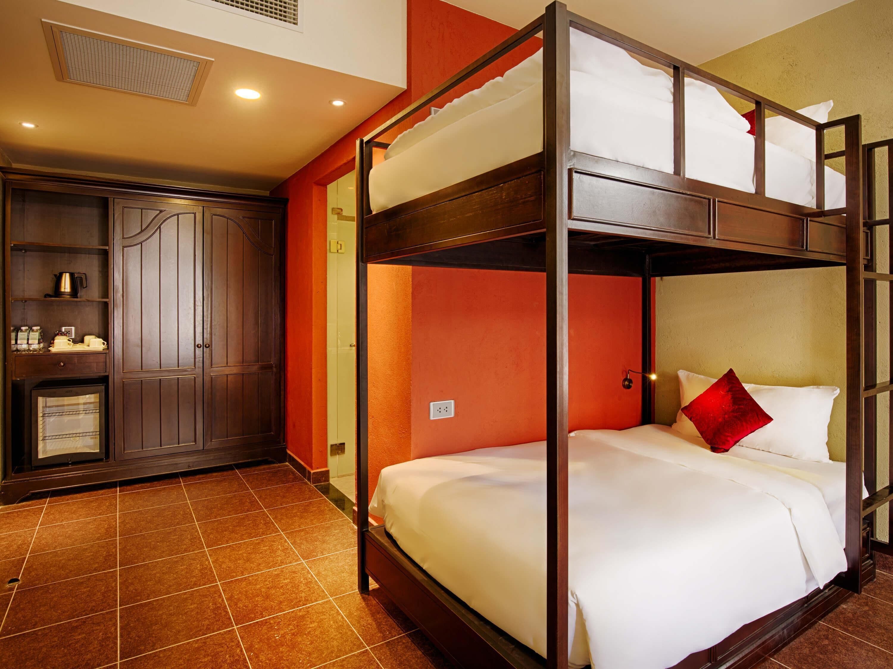 A bunk bed room with a wooden headboard, a wardrobe, and a small kitchenette.